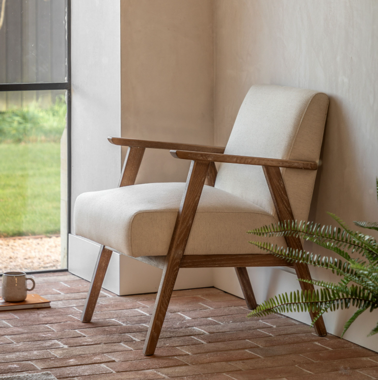 Beige armchair with wooden frame on a wooden floor next to a glass door.