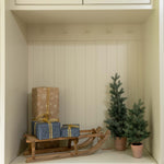 Nook with wooden sled, wrapped presents, and small Christmas trees inside a white cabinet.