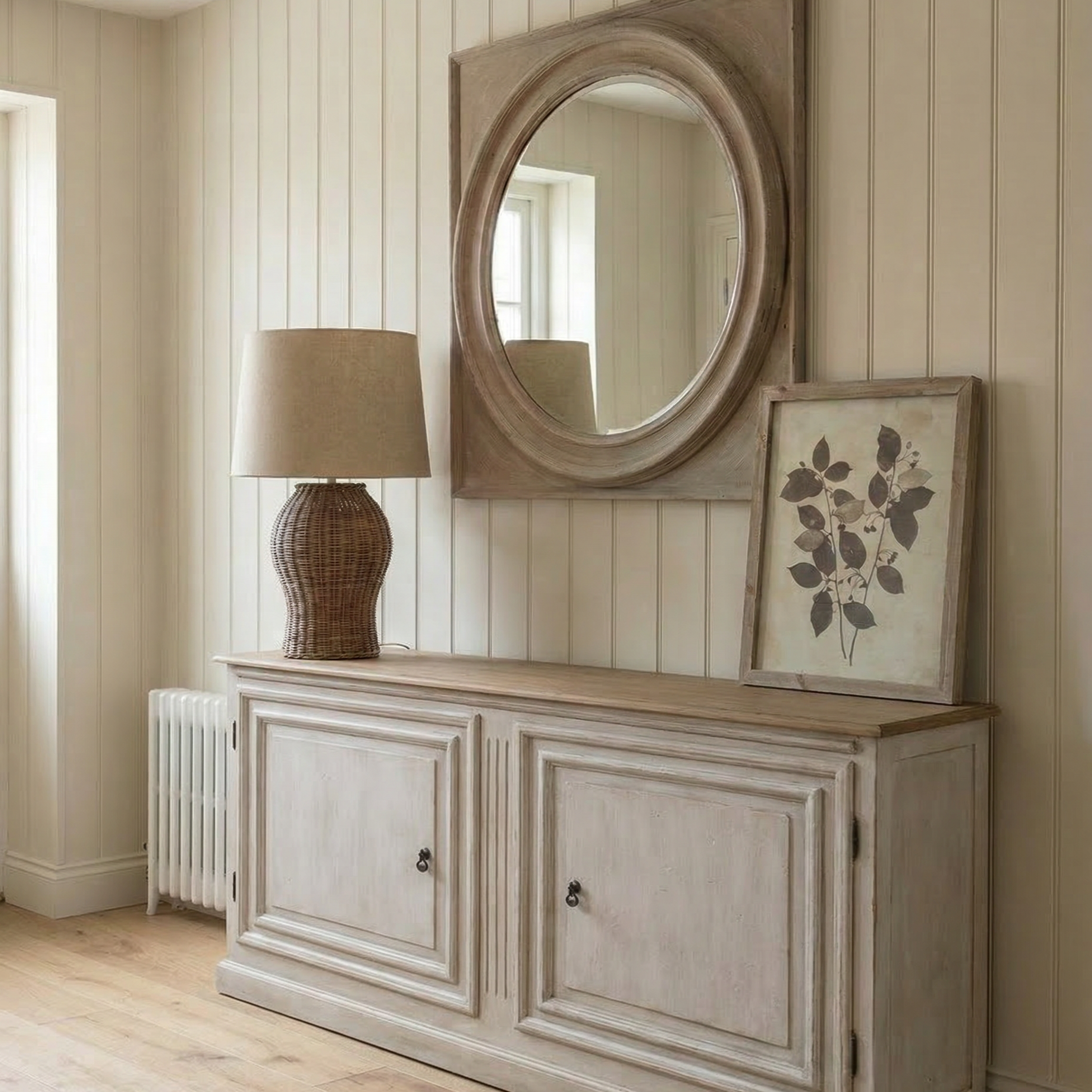 Wooden sideboard with round mirror and lamp against a wall with vertical stripes