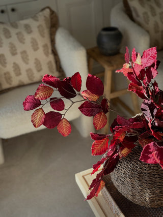 Autumn artificial leaf garland with deep red and orange leaves in a woven basket vase, styled on a side table in a cozy living room.