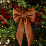 Brown bow ornament on a decorated Christmas tree with lights and red berries.