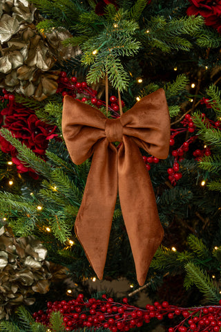 Brown bow ornament on a decorated Christmas tree with lights and red berries.