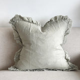 Sage green linen cushion cover with ruffled edges displayed on a light fabric sofa