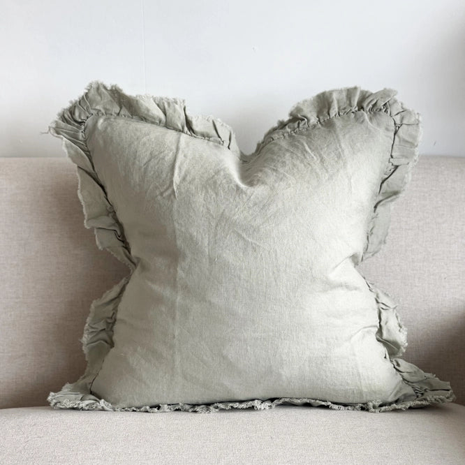 Sage green linen cushion cover with ruffled edges displayed on a light fabric sofa