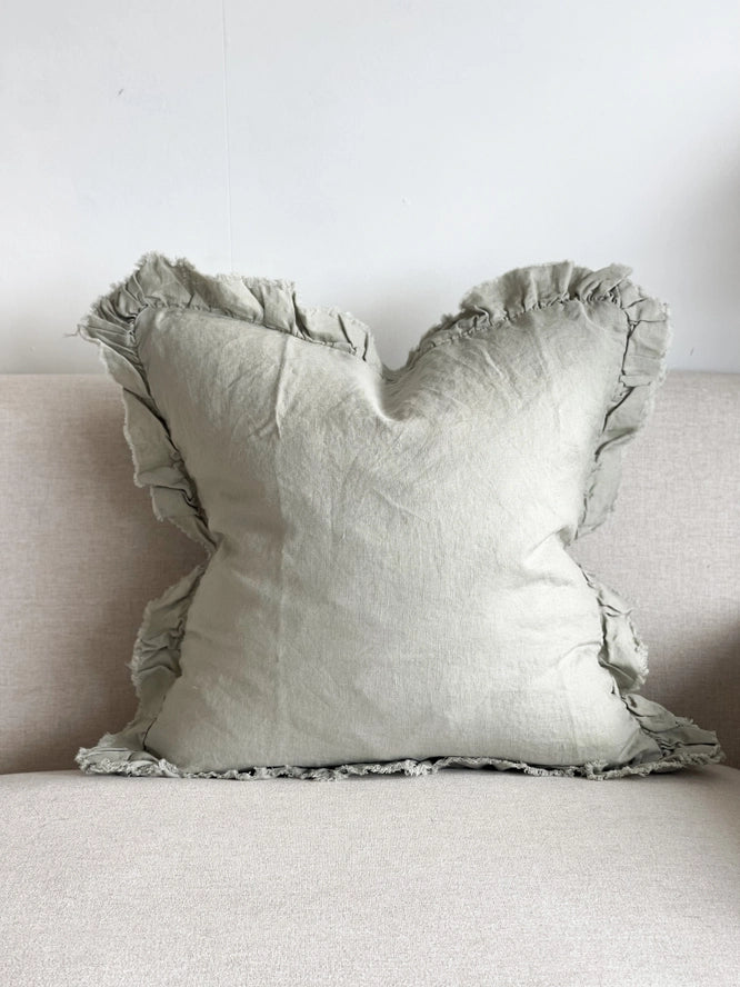 Sage green linen cushion cover with ruffled edges displayed on a light fabric sofa