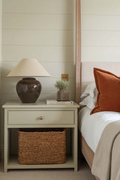 Bedroom with a nightstand, lamp, and decorative items against a wooden paneled wall.