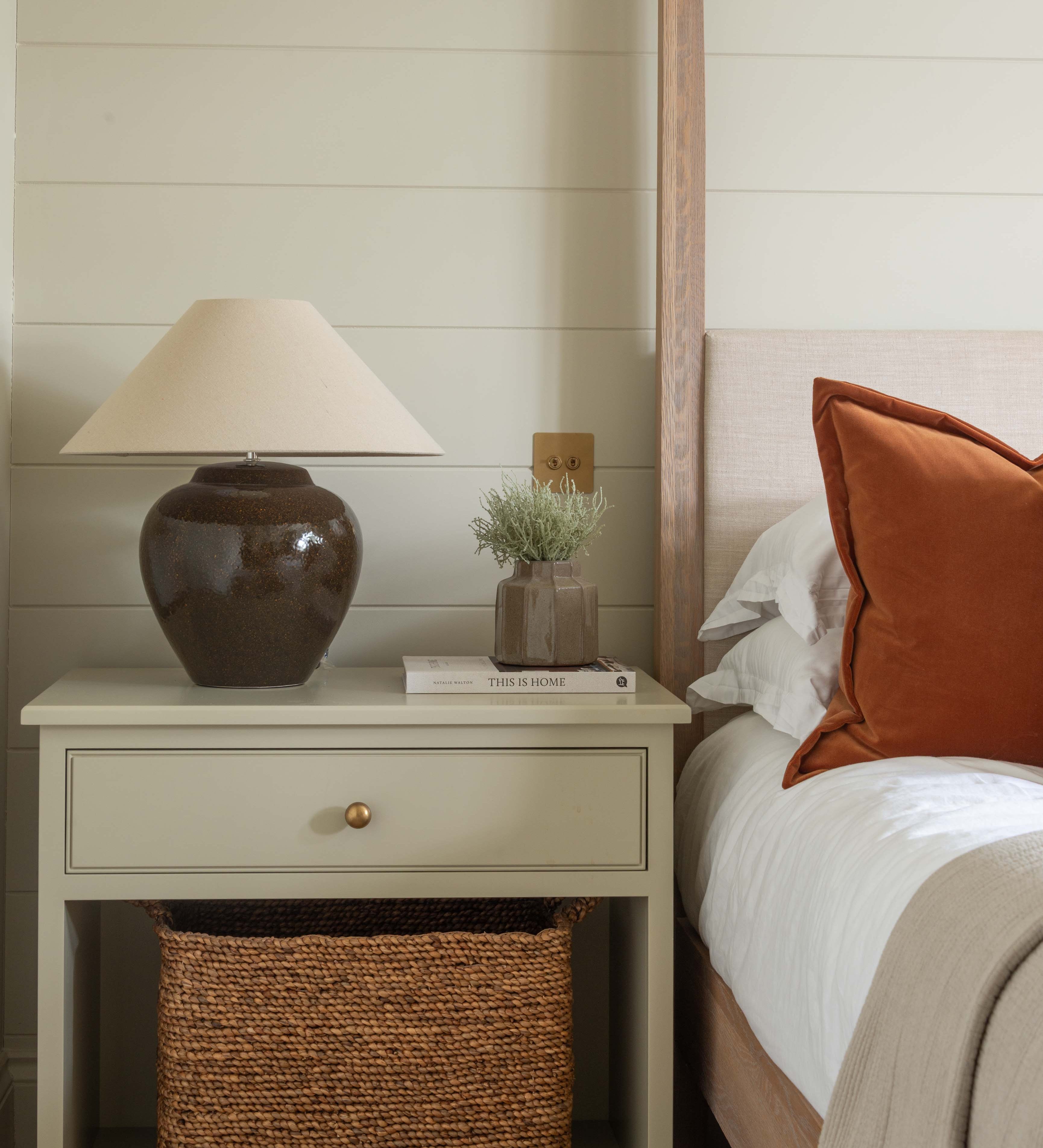 Bedroom with a nightstand, lamp, and decorative items against a wooden paneled wall.