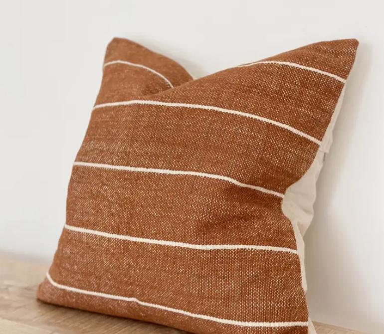 Rust textured cushion cover with ivory horizontal stripes displayed on a wooden surface