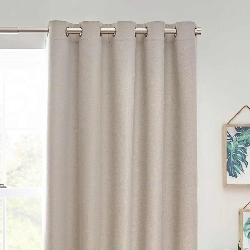 Beige curtain with grommets on a window with a light background