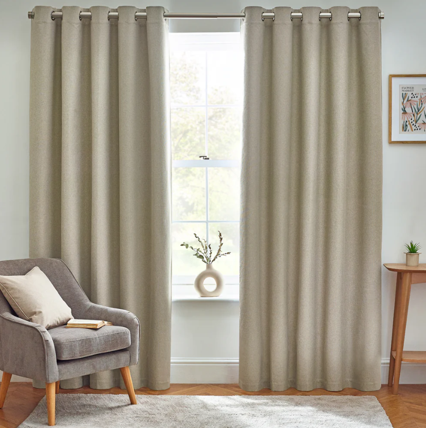 Beige curtains with grommets in a living room setting with a chair and small table.