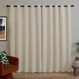 Beige curtains with black grommets in a room with a red chair and abstract art on the wall.
