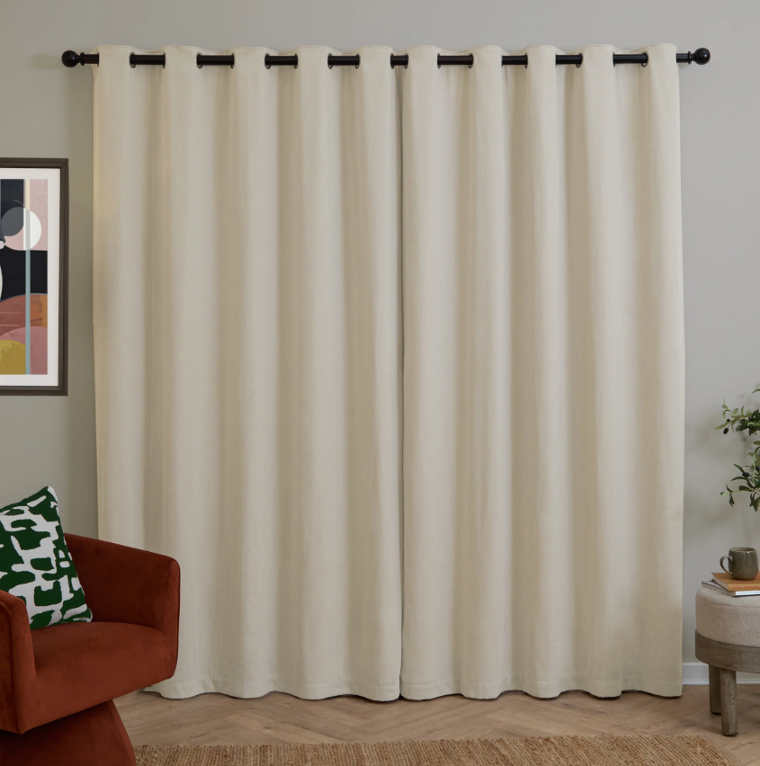 Beige curtains with black grommets in a room with a red chair and abstract art on the wall.