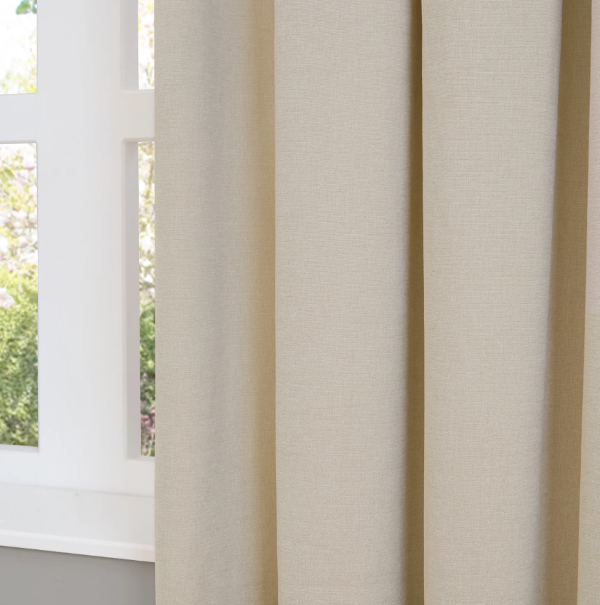Beige curtains partially drawn to reveal a window with greenery outside