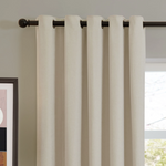 Beige curtains with grommets on a rod in front of a window.
