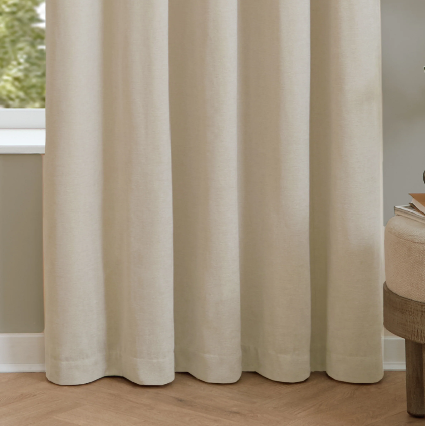 Beige curtains in a room with a wooden floor and a small table.