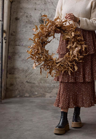 Rustic brown dried leaf wreath held in front of a stone wall