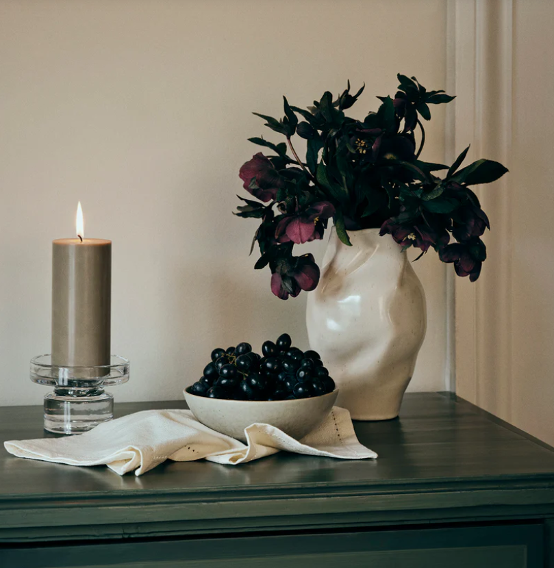 Decorative setup with a vase of flowers, bowl of grapes, and candle on a surface.