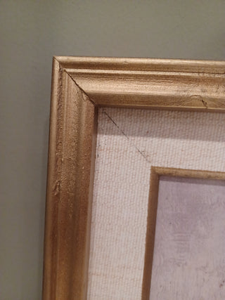 Close-up of a distressed gold picture frame with a textured off-white mat board, shown against a neutral gray wall.