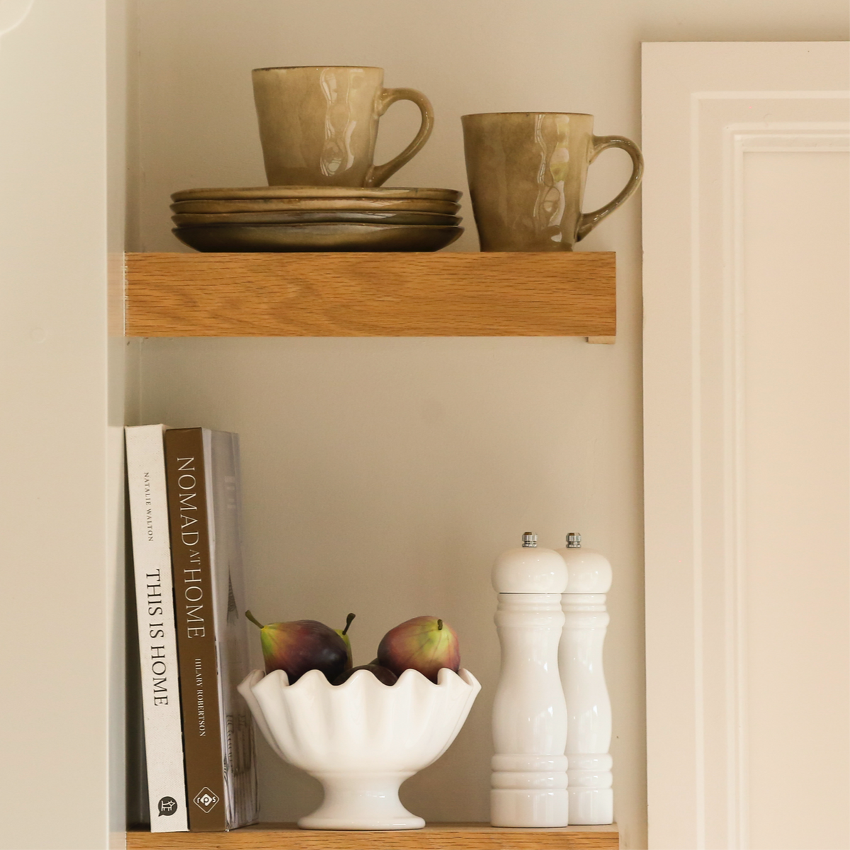 stoneware side plates stacked on a wooden shelf alongside mugs and home décor accessories