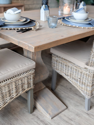 Dining table set with plates, glasses, and cutlery on a wooden floor with wicker chairs.