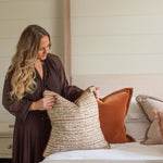 Woman arranging pillows on a bed in a bedroom setting