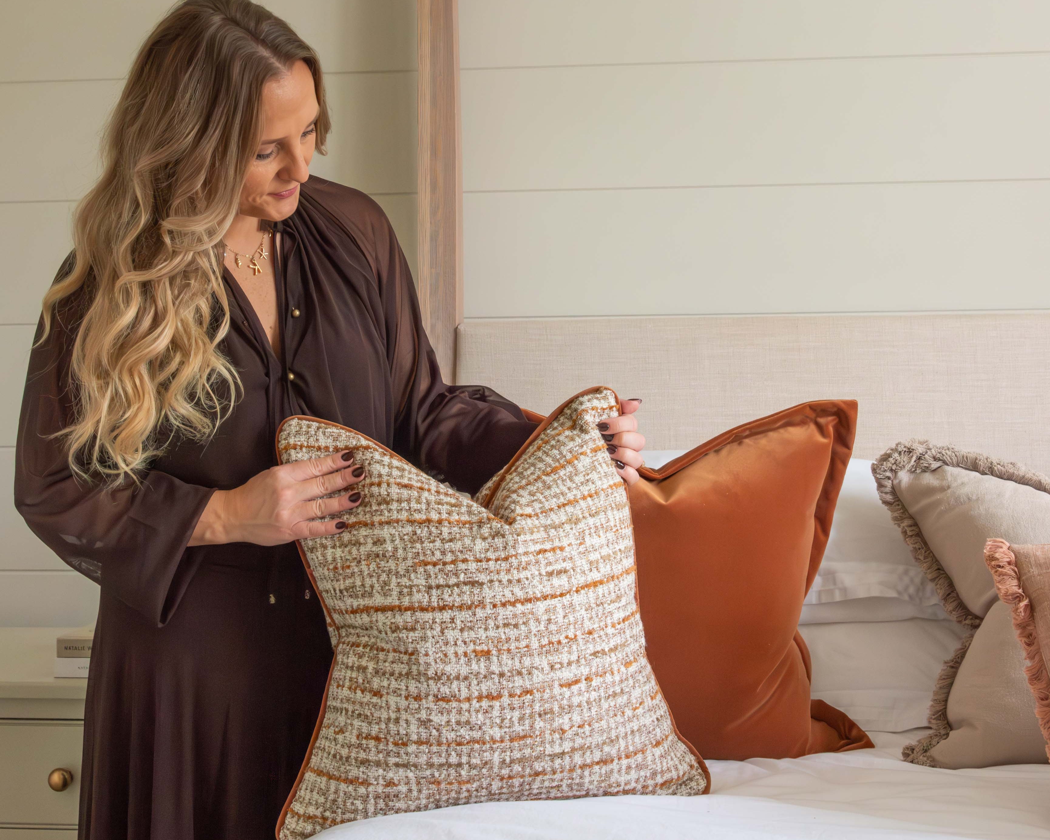 Woman arranging pillows on a bed in a bedroom setting