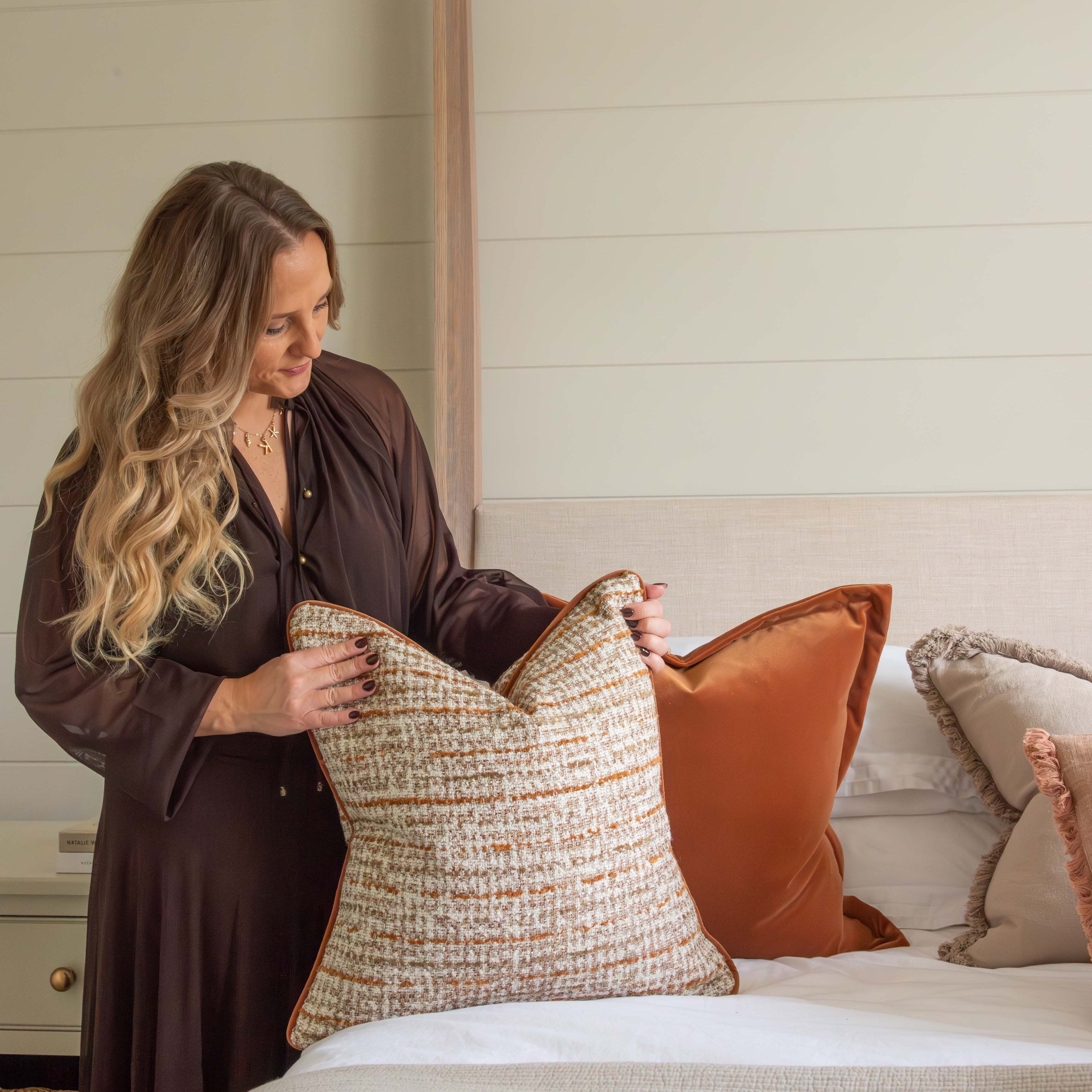 Woman arranging pillows on a bed in a bedroom setting