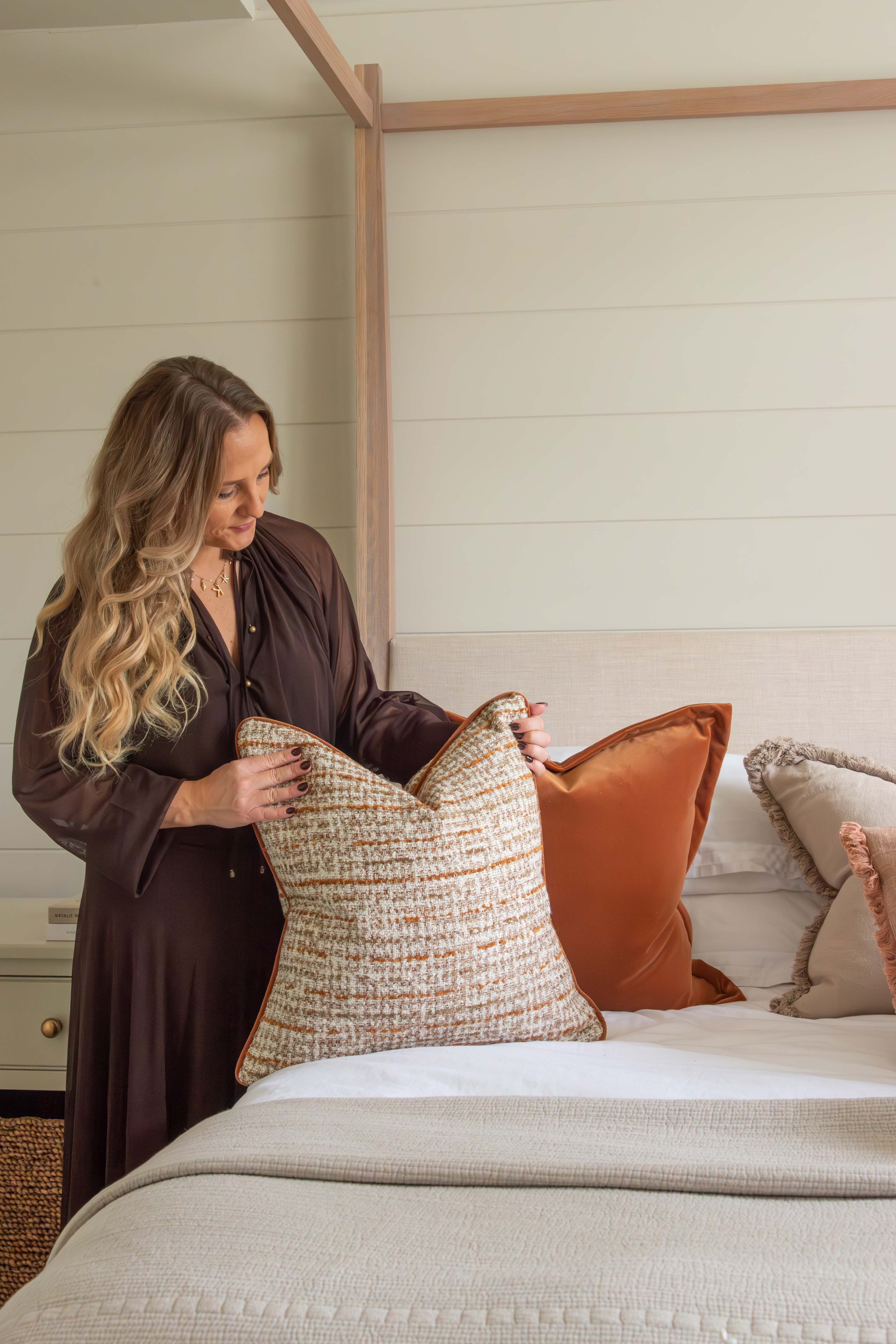 Woman arranging pillows on a bed in a bedroom setting