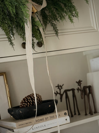 Close up of faux cedar garland tied with a cream ribbon above a styled shelf