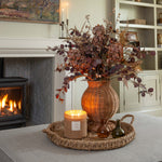 Autumn artificial floral arrangement with figs and candle by fireplace