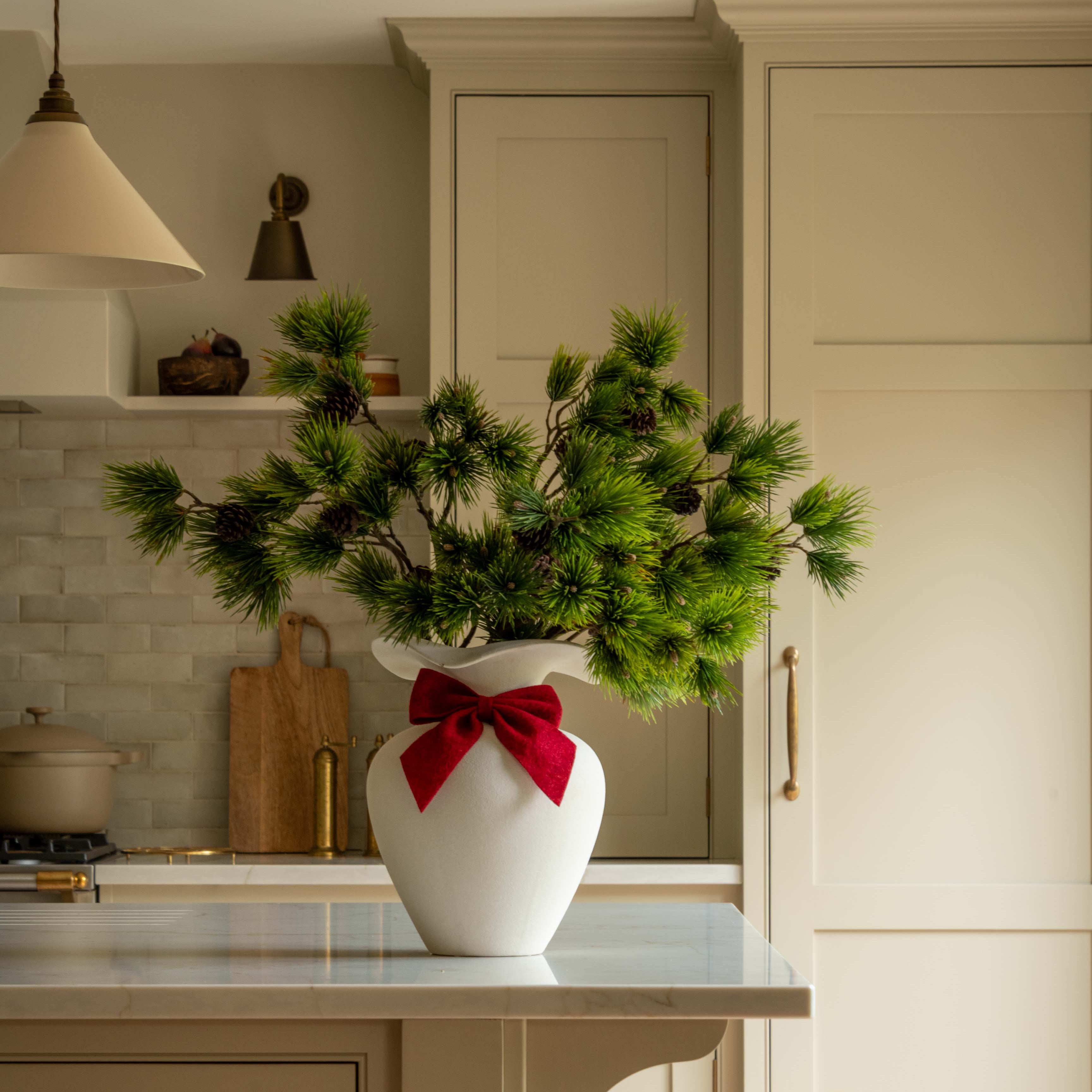 Kitchen with a vase of greenery and a red bow on a white countertop.