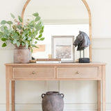 A stunningly crafted brass-framed arched top mirror. It sits on a pine console table.