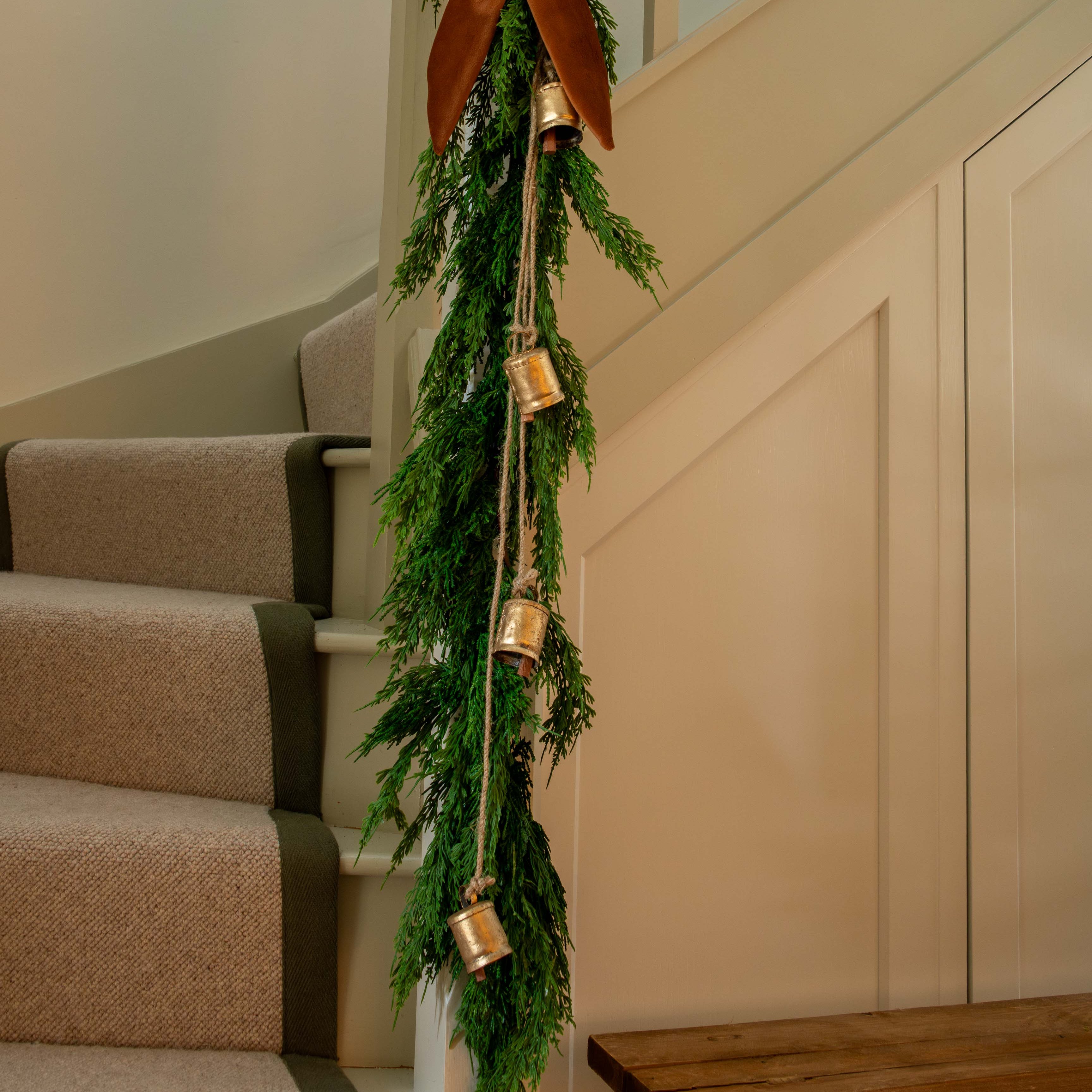 Vintage brass bell cluster hanging on natural jute string with greenery and bow on staircase railing