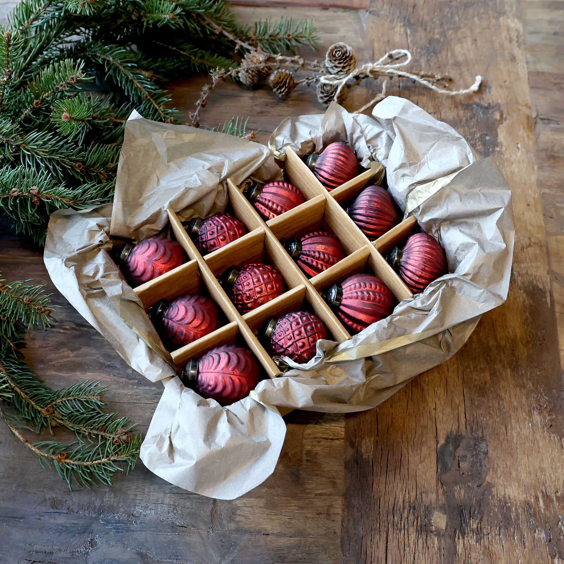 Set of 12 vintage red glass baubles in storage box with Christmas tree branches on wooden table