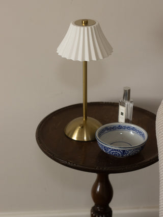 Small table with a lamp, bowl, and bottle against a plain wall
