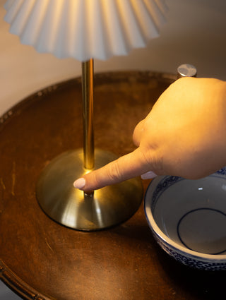 Hand adjusting a lamp on a wooden surface with a bowl in the foreground