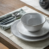 Set of white ceramic bowls on a wooden table with cutlery and a napkin.