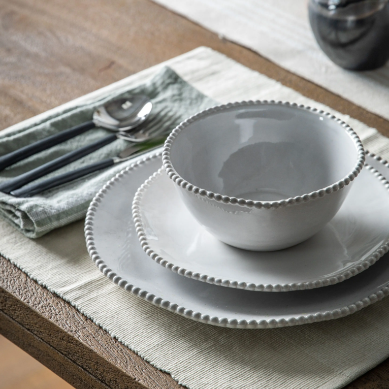 Set of white ceramic bowls on a wooden table with cutlery and a napkin.