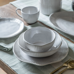 White ceramic dinner plate with ribbed detailing and soft rippled edge on a table setting