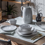 White ceramic pasta bowl with ribbed detailing and wide shallow shape on a table setting