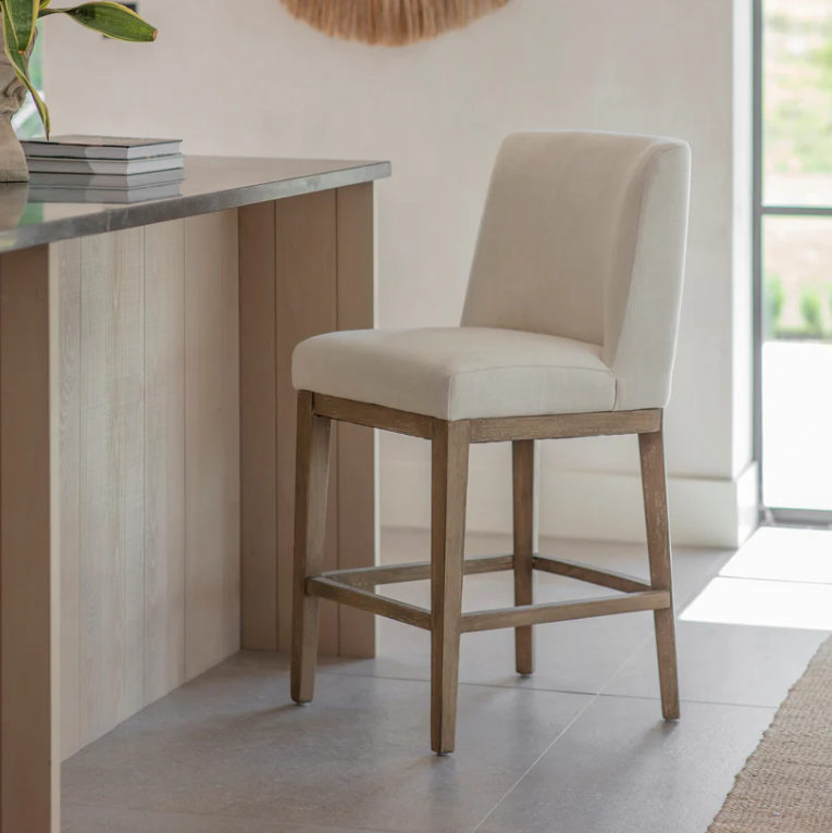 Linen upholstered counter stool with solid wood legs positioned at a modern kitchen island
