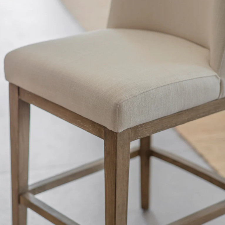 Linen upholstered counter stool with solid wood legs positioned at a modern kitchen island