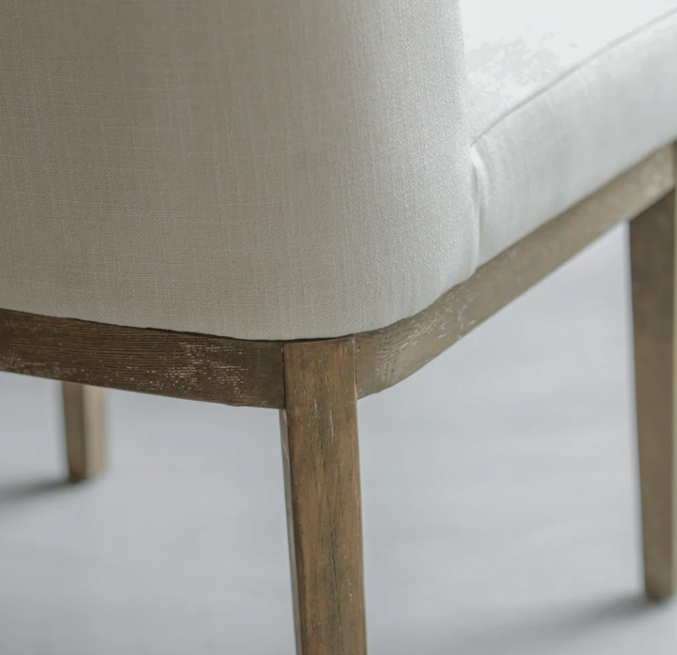 Close-up of a chair with wooden legs and beige cushioned seat on a light background