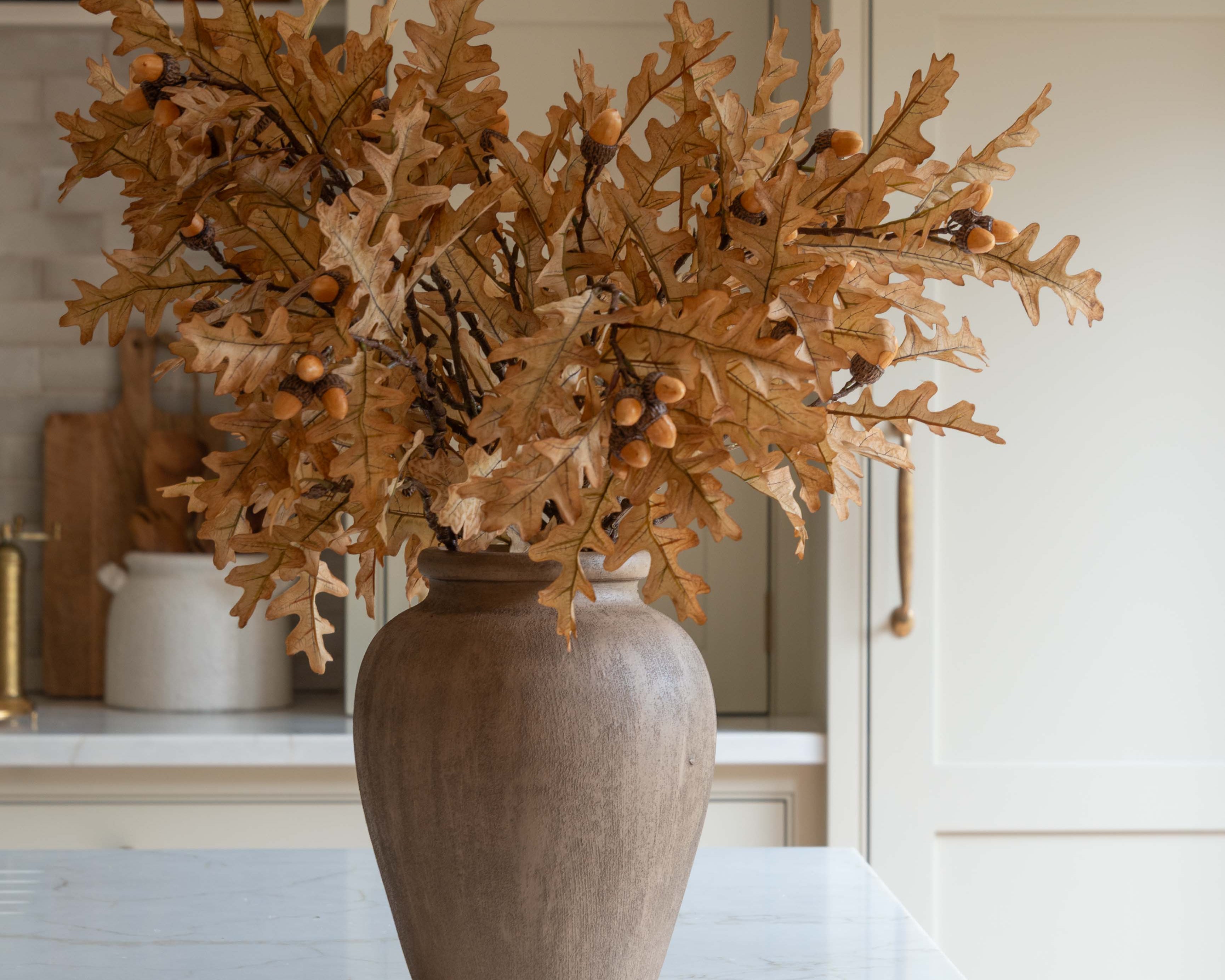 Close-up of Charles Ted Faux Oak Leaves with Acorns in a decorative vase on a kitchen island