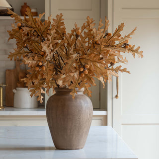 Faux oak leaves with acorns arranged in a tall vase, bringing golden autumn tones to a kitchen