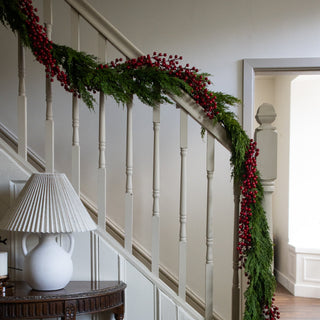 Crimson berry garland wound through greenery along a white staircase banister