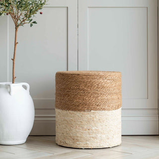 Coastal Charm handwoven footstool in natural maize and rush with two-tone tan and cream cylindrical drum design, styled beside a white ceramic vase