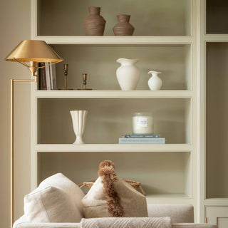 Bookshelf with decorative items including vases and a candle, with a gold lamp on a beige wall.