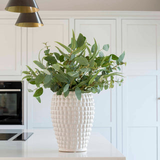 White textured vase with green leaves on a kitchen counter