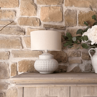White textured lamp on a wooden shelf against a stone wall